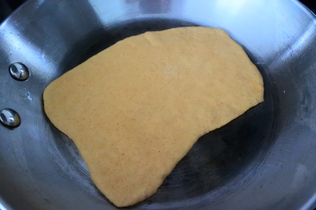 An angled image of the uncooked side of a naan in a skillet