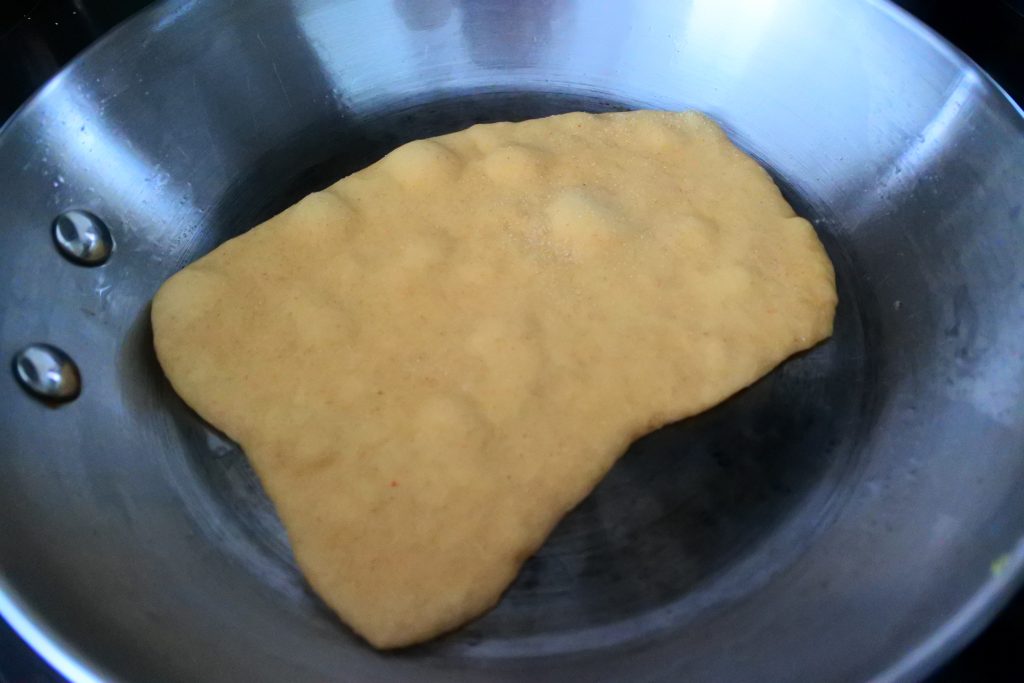 An angled image of the uncooked but bubbled side of a naan in a skillet