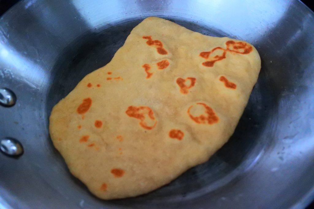 An angled image of a cooked naan in a skillet