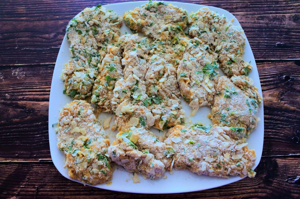 An angled image of uncooked herb crusted parmesan chicken cutlets on a plate
