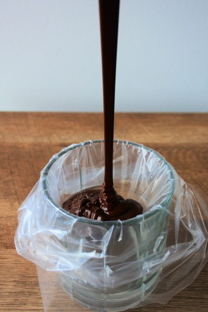 A head on image of a pastry bag in a glass being filled with melted dark chocolate