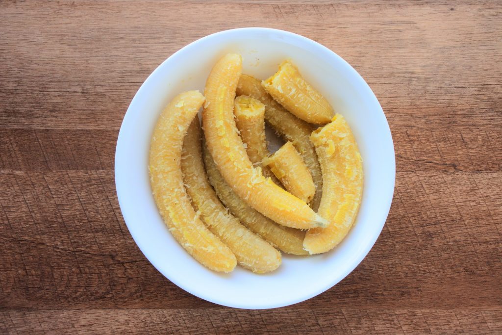 An overhead image of whole, peeled green bananas in a bowl
