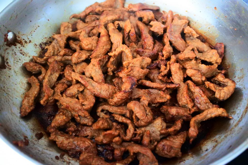 An angled image of caramelized thinly sliced marinaded beef in a pan