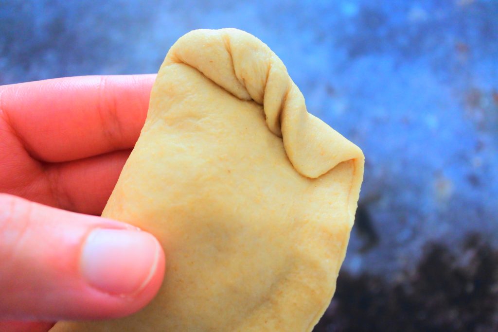 A closeup image of an uncooked potato stuffed pie illustrating how the edges are twisted and folded