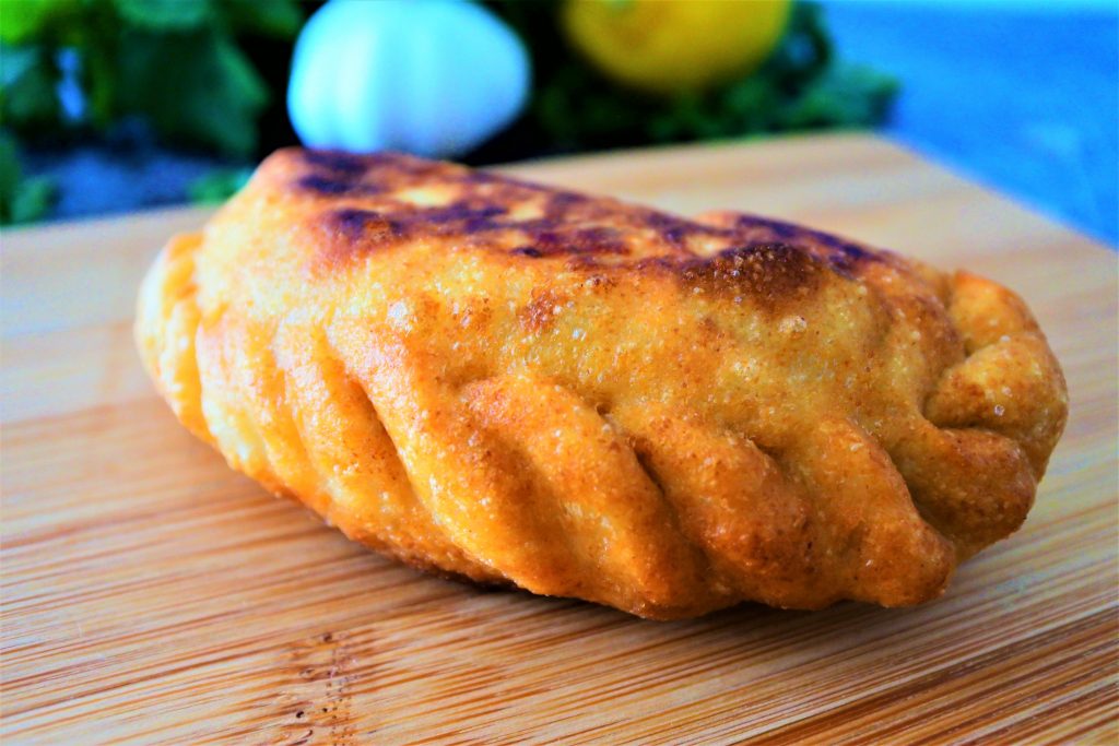 A close up image of a golden fried potato samosa/ aloo pie on a wooden plank