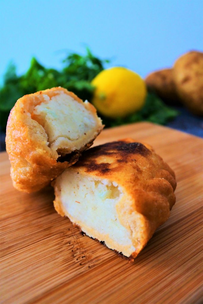 A close up image of a golden fried potato samosa / aloo pie cut in half on a wooden plank