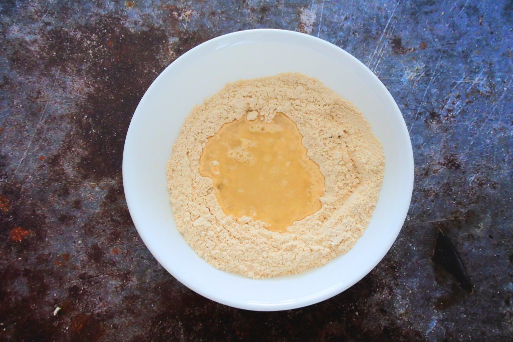 An overhead image of a bowl of flour with water added to it for a dough