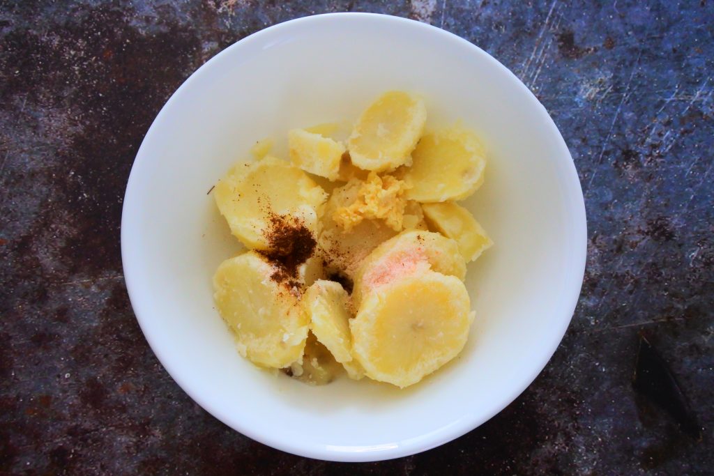 An overhead image of a bowl of sliced and boiled potatoes topped with seasoning