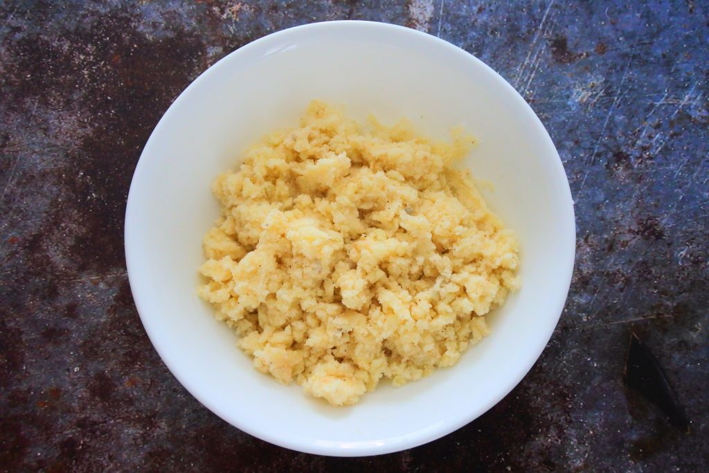An overhead image of a bowl of mashed and seasoned potato