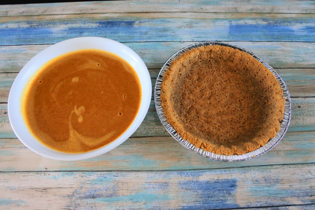 An angled overhead image of a bowl containing pumpkin pie filling next to a prebaked pie crust in a pie tin