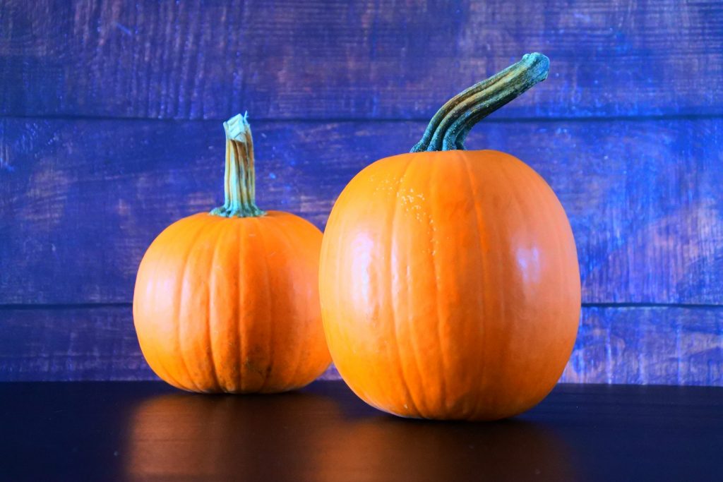 A head on image of two pumpkins on a black surface with a wooden background