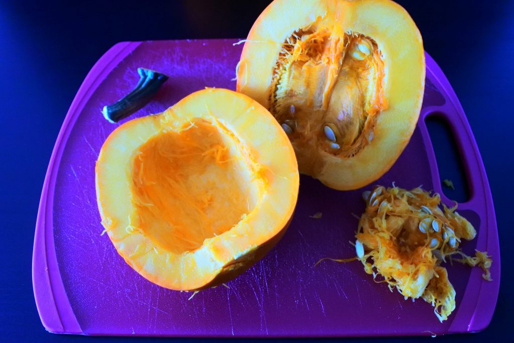 An angled image of a pumpkin cut in half with the insides of one half scraped out on a cutting board