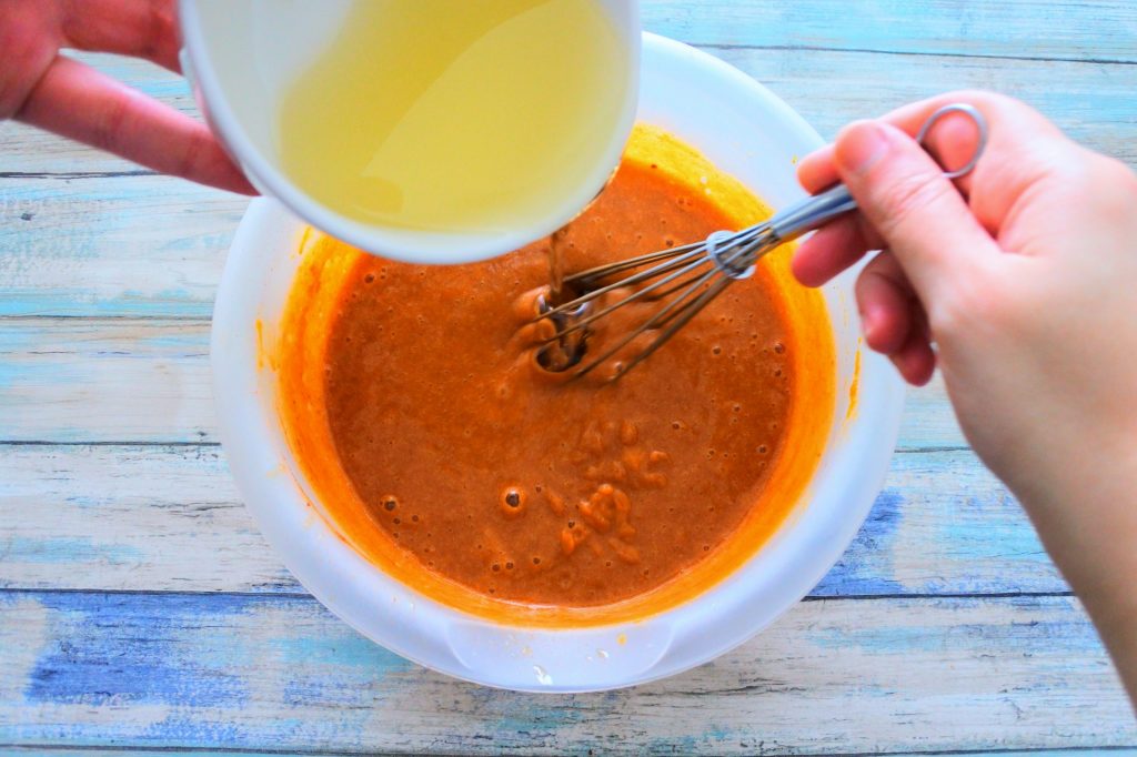 An overhead image of extra light olive oil being poured into the bowl with batter for pumpkin spiced loaf
