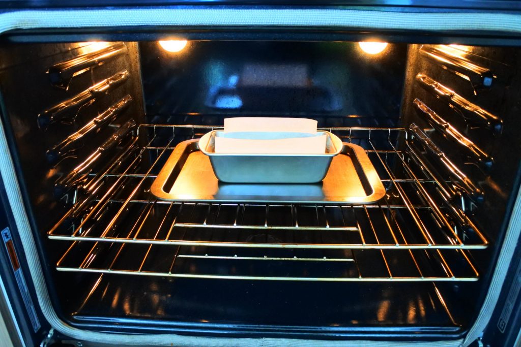 A head on image of a loaf pan of pumpkin spice bread on a baking tray in the oven on a rack one spot lower than the middle