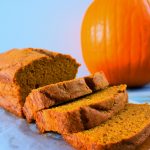 A head on image of sliced pumpkin spice loaf on a board next to a pumpkin