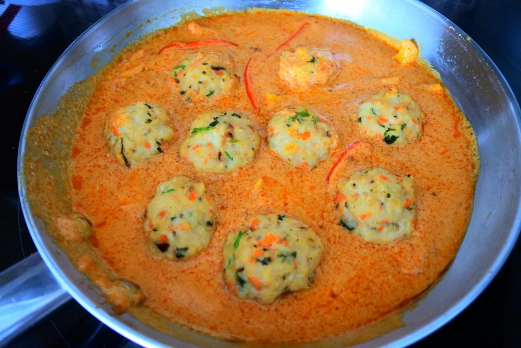An overhead image of a pan of red thai curry with peppers and thai chicken meatballs