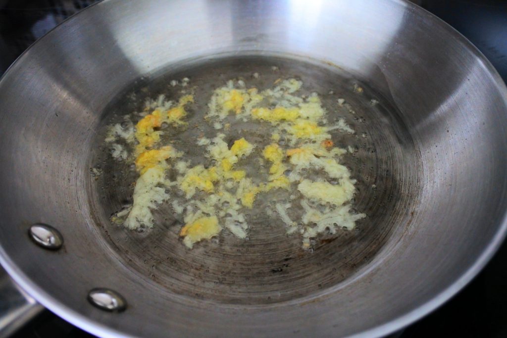 An overhead image of a pan with garlic and ginger being fried in oil