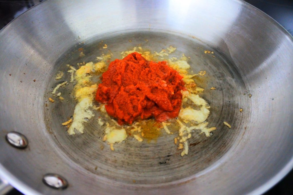 An overhead image of a pan of spices in oil with red curry paste