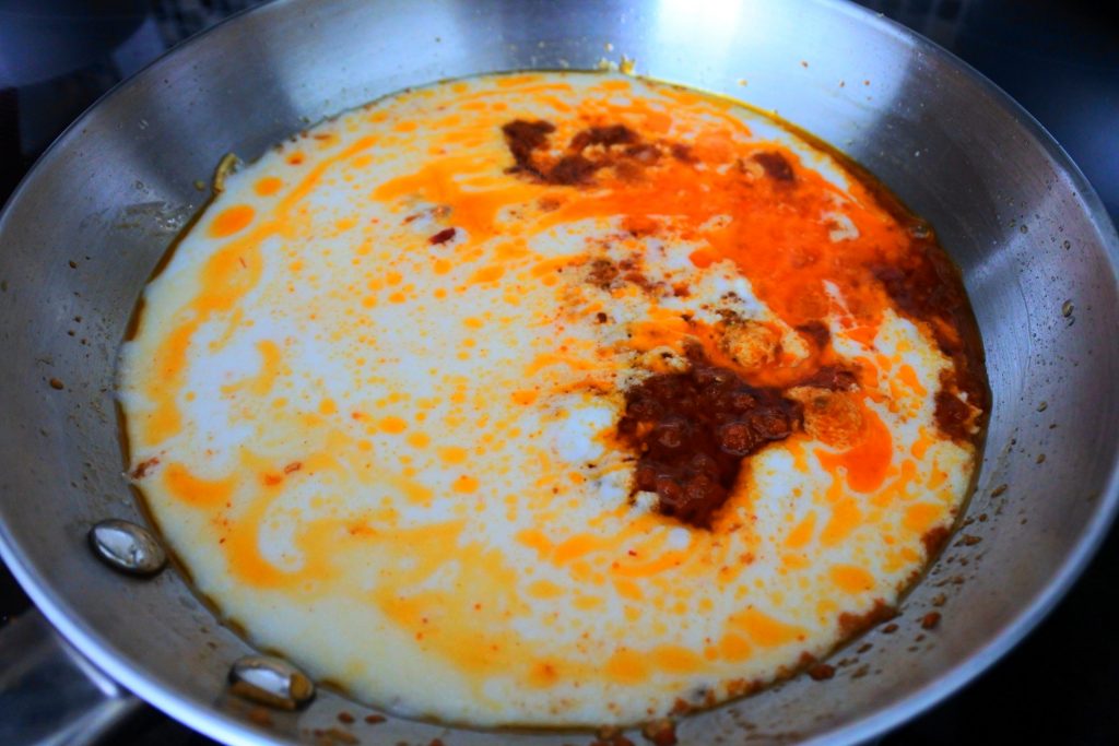 An overhead image of a pan with simmering red curry paste, spices, and coconut milk