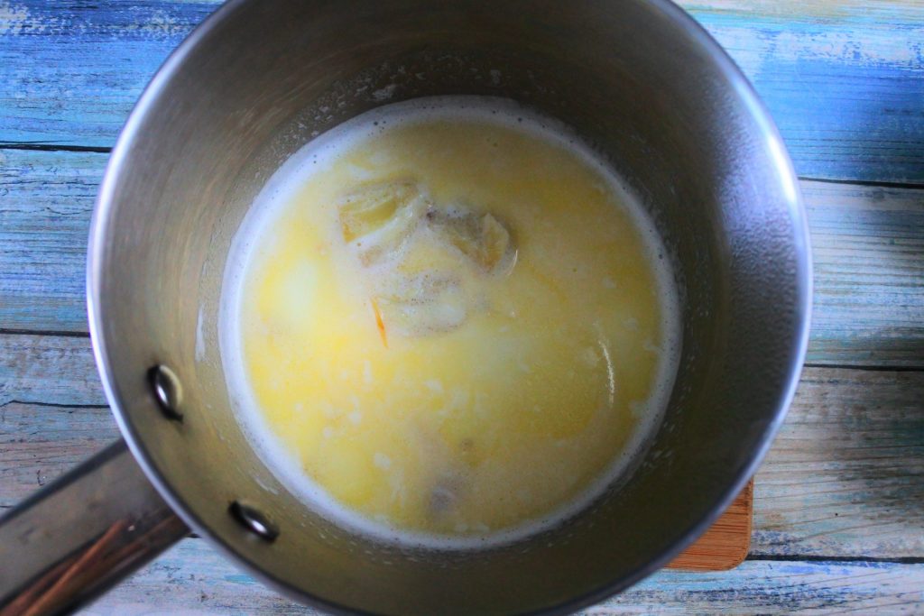 An overhead image of a pot with warmed milk, melted butter, and roasted garlic cloves