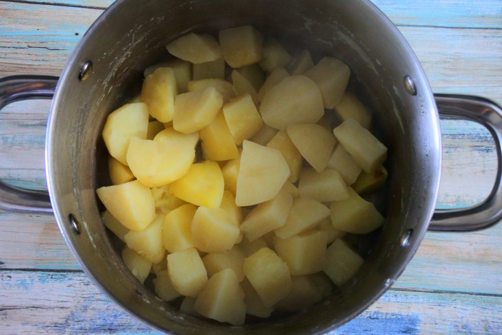An overhead image of a pot with cubes of peeled and cooked potatoes