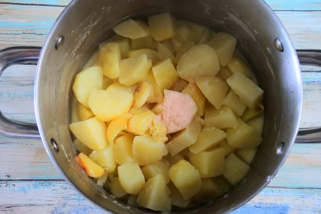 An overhead image of a pot of boiled, cubed potatoes with a roasted garlic, salt, milk and butter mixture added in