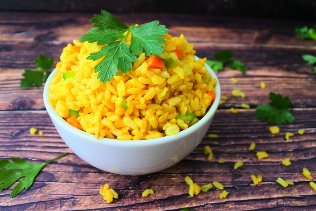 A close up image of a bowl of saffron rice with diced carrots and green bell peppers mixed in and a garnish of fresh parsley