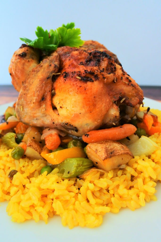 An image of a cornish game hen on a bed of vegetables and some coconut saffron rice