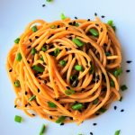 An overhead image of a plate of sesame noodles topped with chives and black sesame seeds