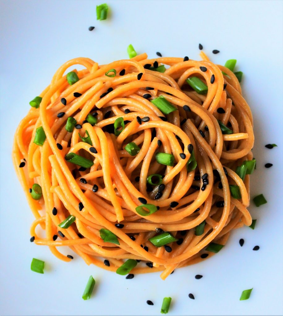 An overhead image of a plate of sesame noodles topped with chives and black sesame seeds