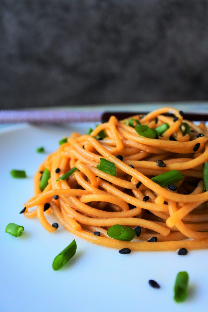 A head on image of a plate of sesame noodles topped with chives and black sesame seeds