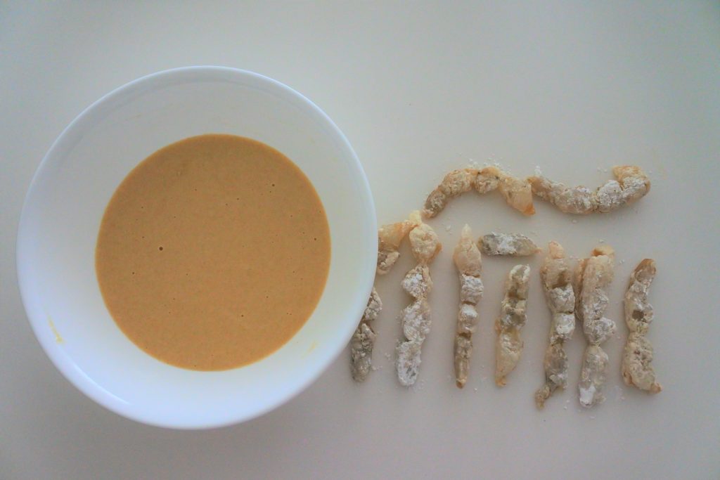 An overhead image of straightened shrimp dusted in potato starch next to a bowl of tempura batter
