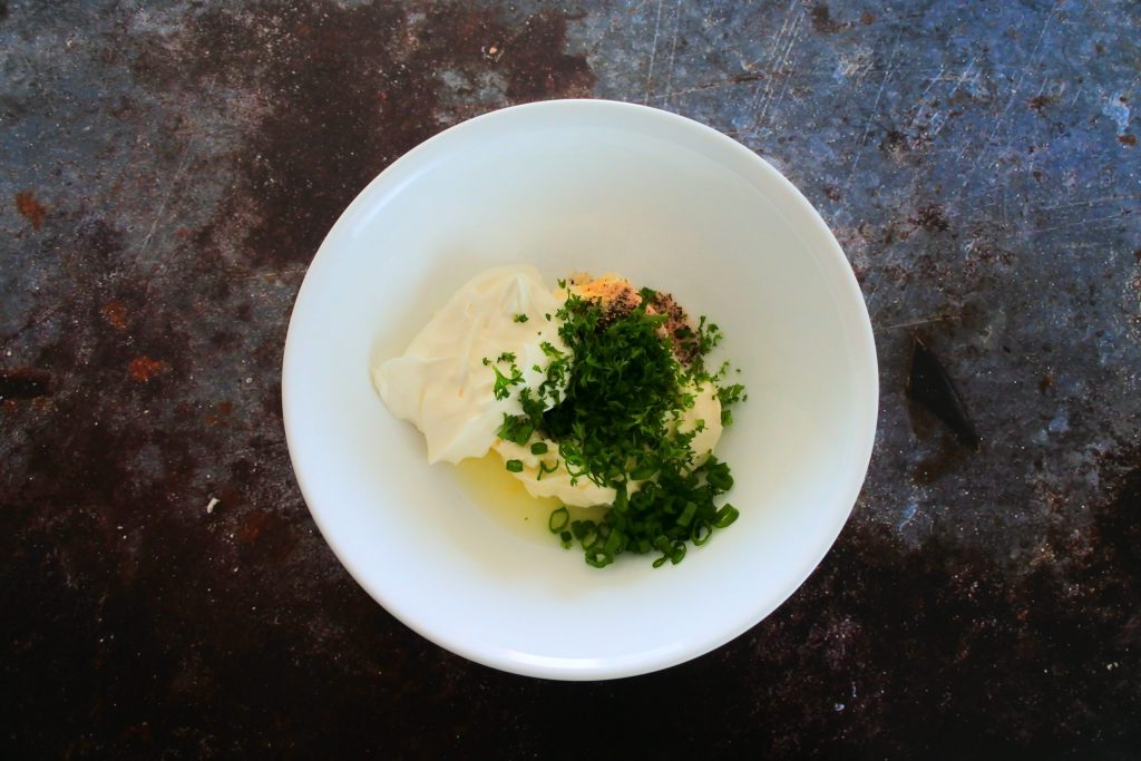 An overhead image of a bowl with mascarpone cheese, sour cream, spices, lemon juice and fresh herbs