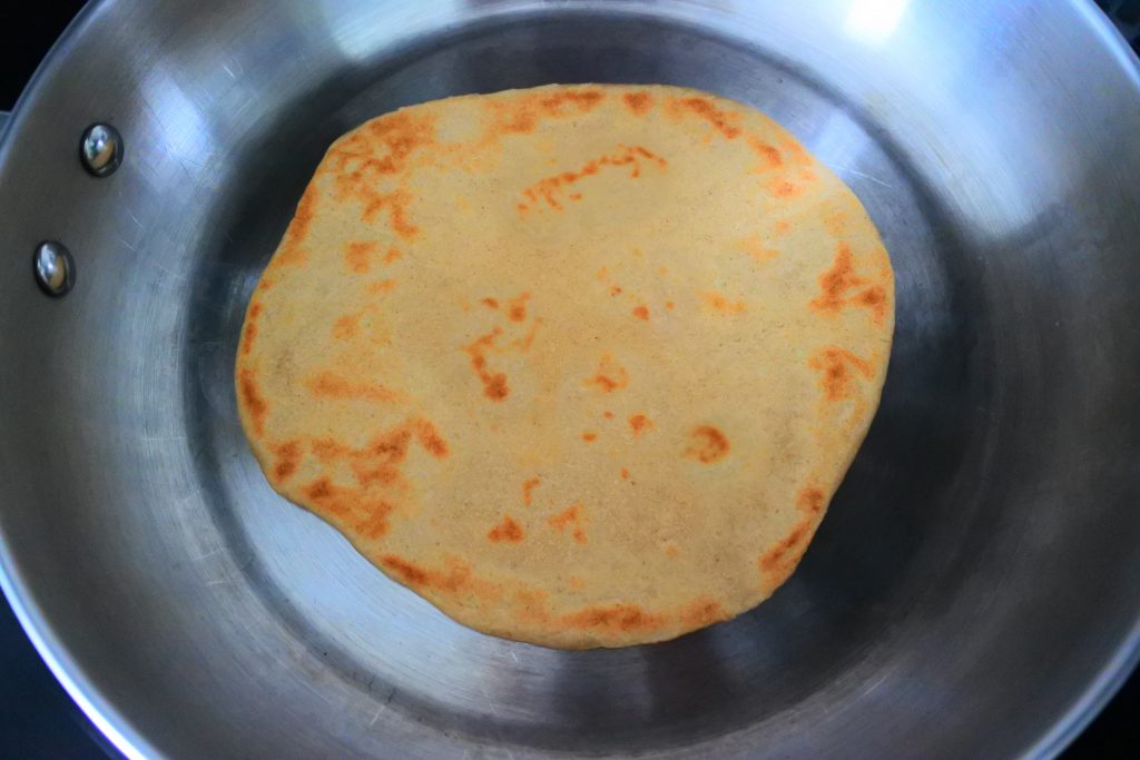 An overhead image of a flipped whole wheat tortilla cooking in a skillet