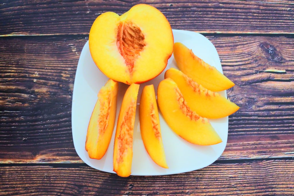 An angled image of a plate containing a ripe half cut fresh peach and several peach slices