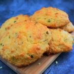 A close up image of a stack of sour cream and chive cheddar biscuits on a wooden plank