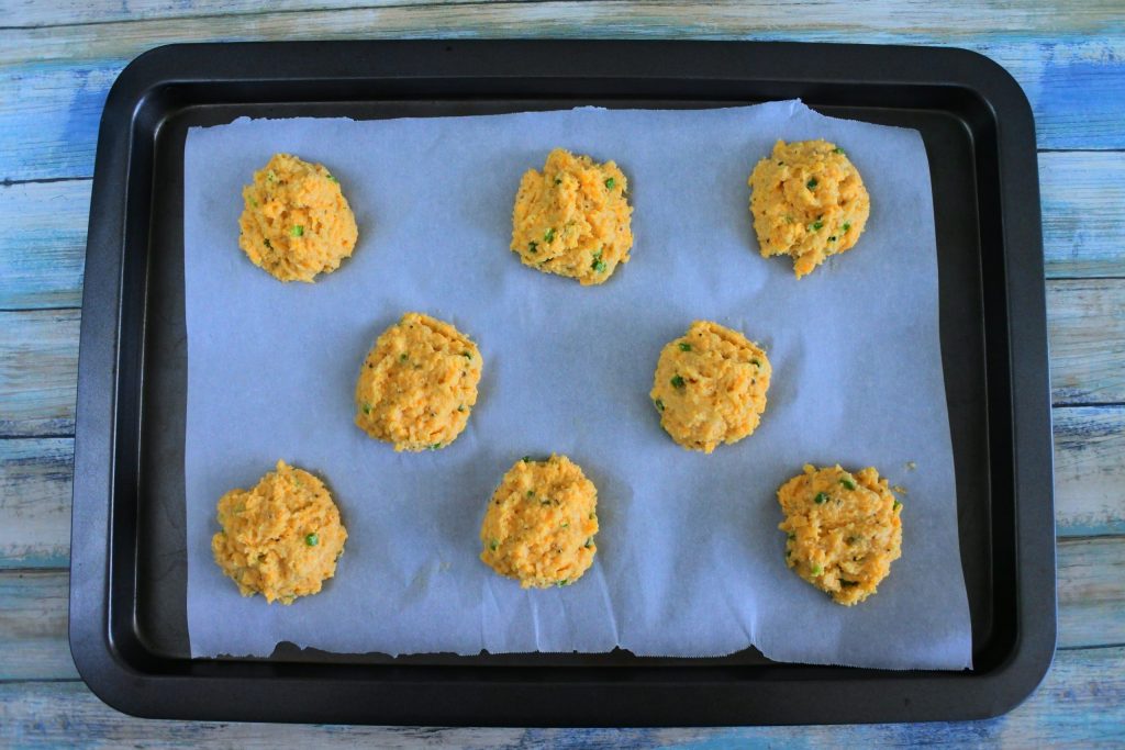 An overhead image of a parchment lined tray with unbaked sour cream and chive cheddar biscuits