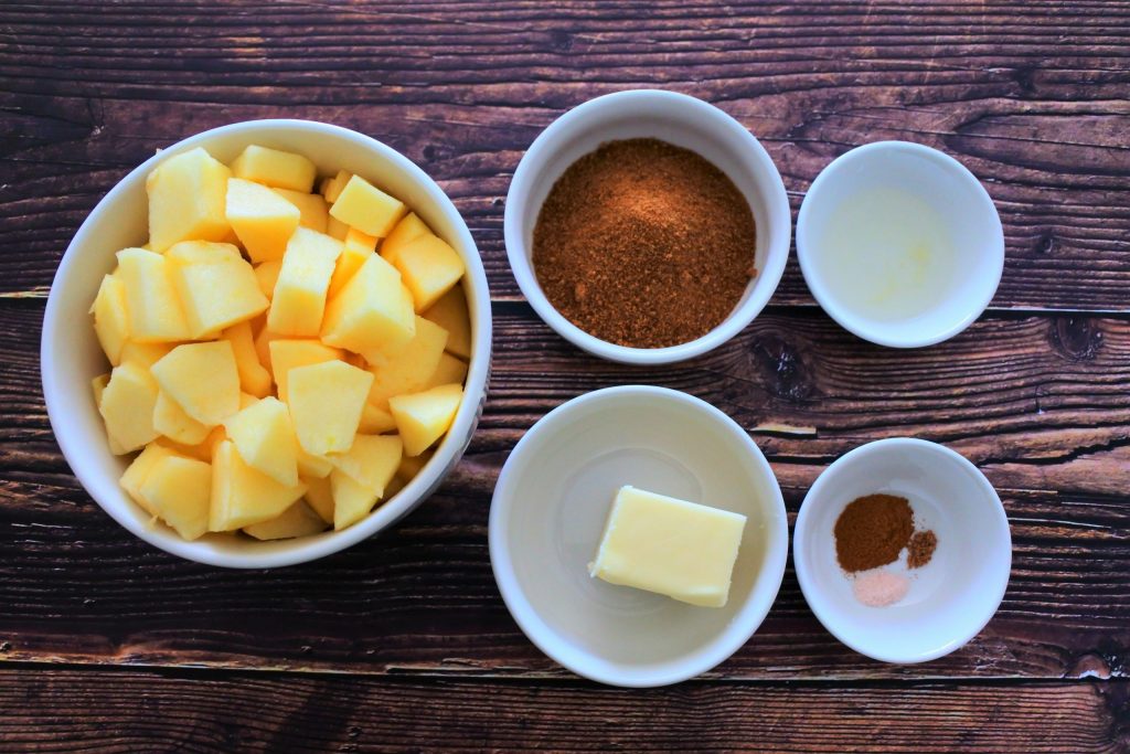 An overhead image of bowls of ingredients for Southern Fried Apples including fresh apple chunks, coconut sugar, lemon juice, butter and spices including salt, nutmeg and cinnamon