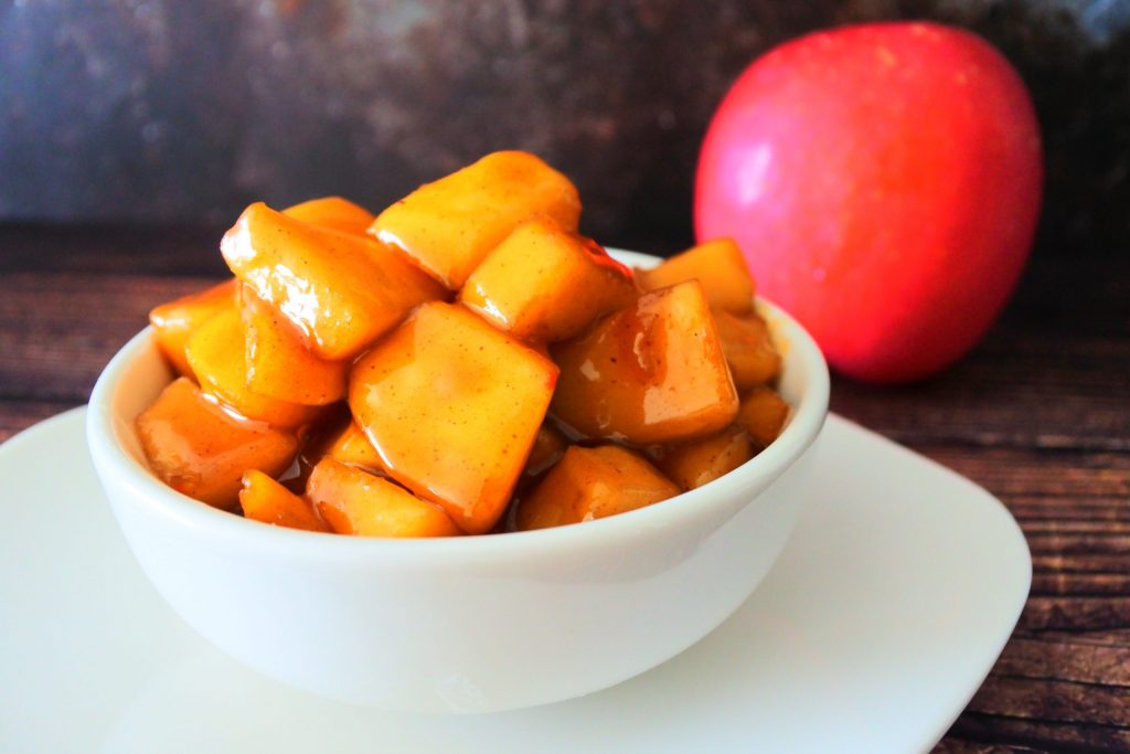 A head on close up image of Southern Fried Apples in a white bowl with a whole red apple in the background