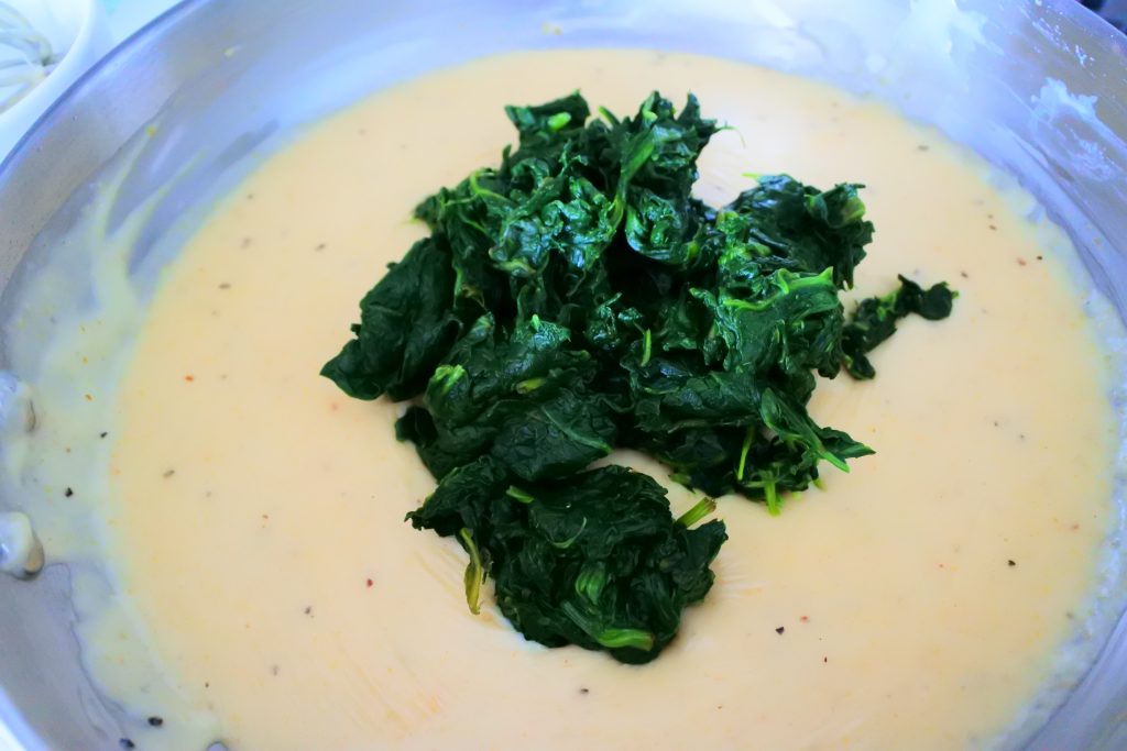 A close up image of a thickened, cheesy roux sauce with a pile of steamed spinach in the middle