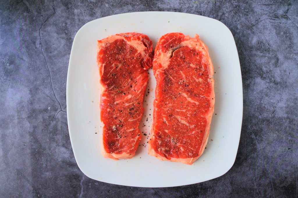 An overhead image of salt and pepper seasoned steaks on a plate