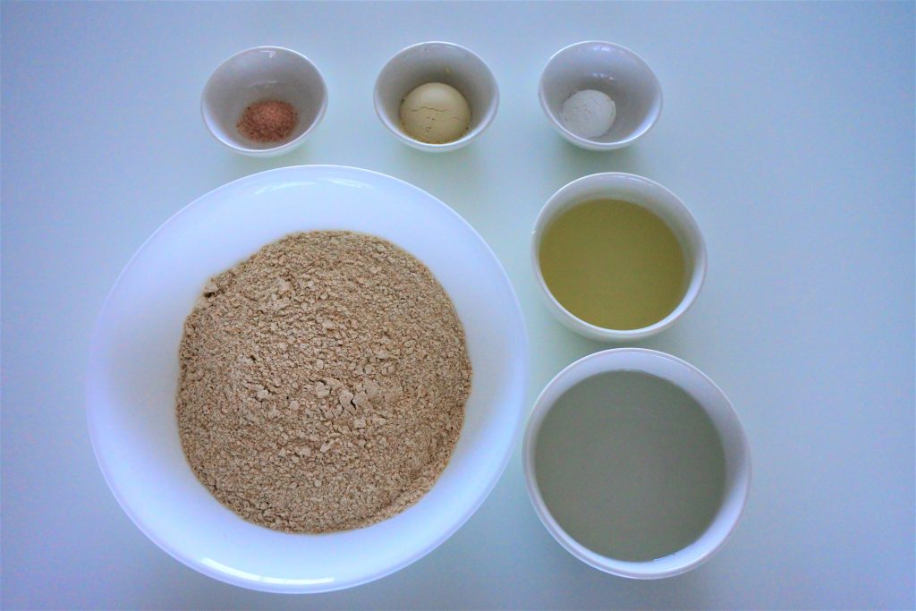 An overhead image of bowl containing the following ingredients: Himalayan salt, vital wheat gluten, baking powder, white whole wheat flour, oil and water
