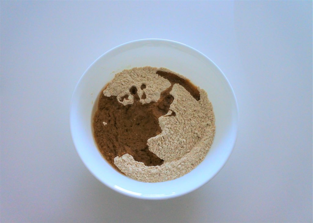 An overhead image of a bowl of white whole wheat flour with a layer of oil on top