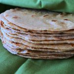 Close up image of a stack of whole wheat flour tortillas wrapped in a green linen napkin