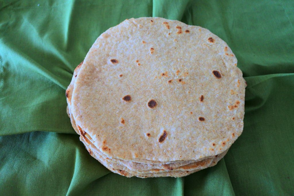 Overhead image of a stack of whole wheat flour tortillas sitting on top of a green linen napkin